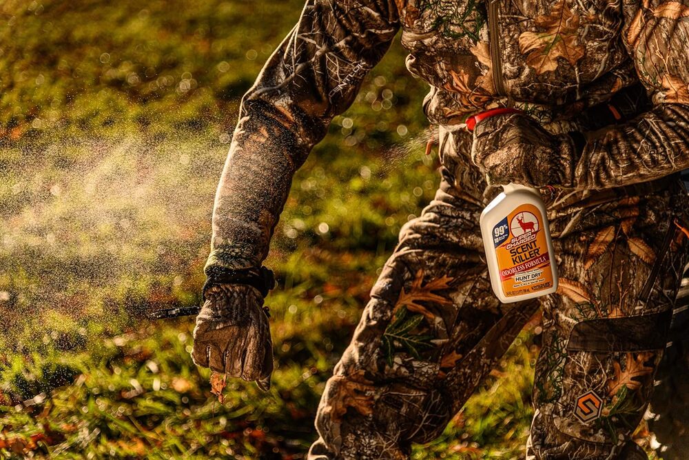 Person in camouflage holding a bottle of Bear Balm in a forest setting