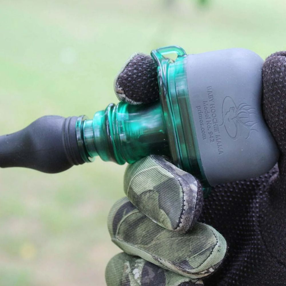 Close-up of a green water bottle with a gray cap held by a gloved hand against a blurred natural background.