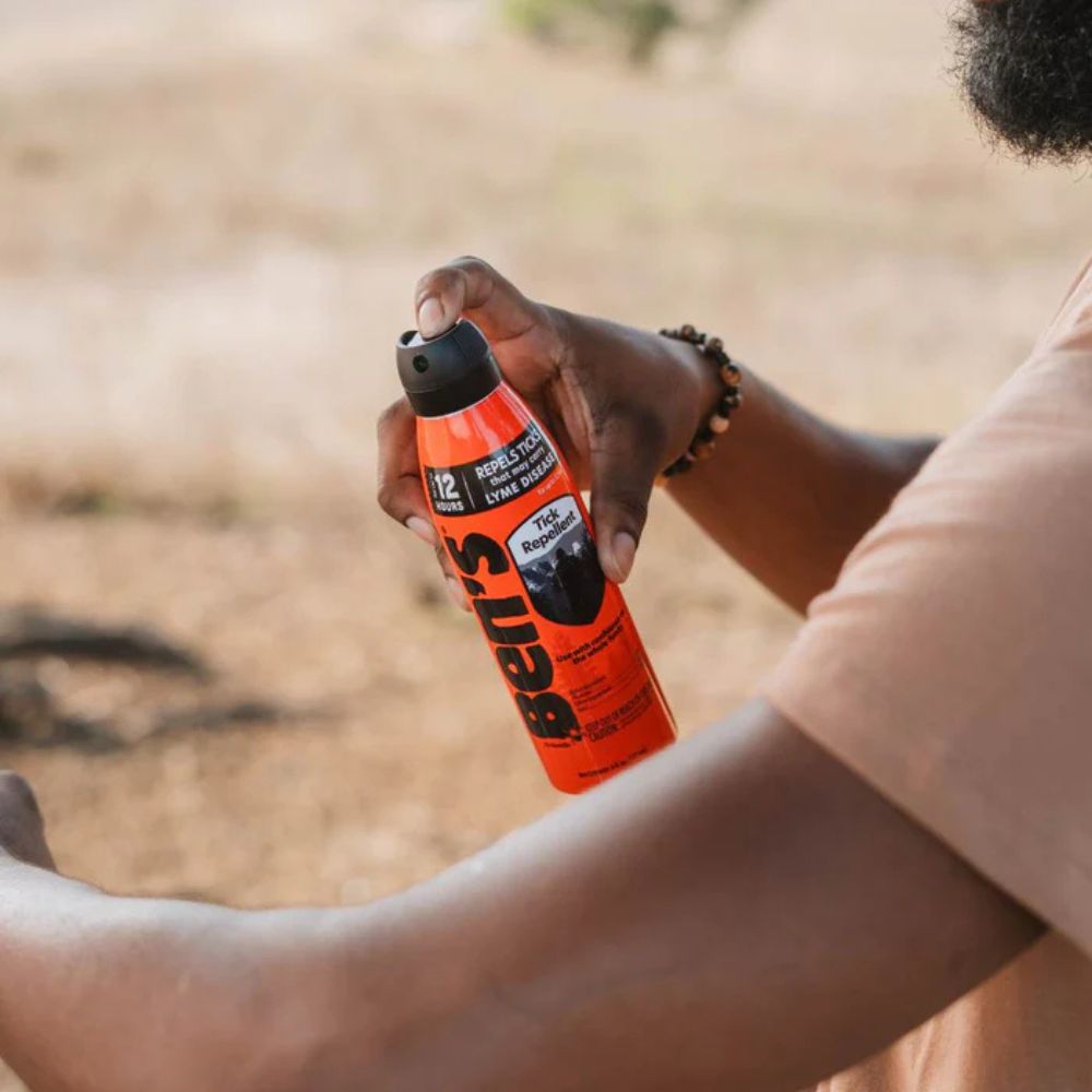 Person holding a can of Belts insect repellent spray outdoors.