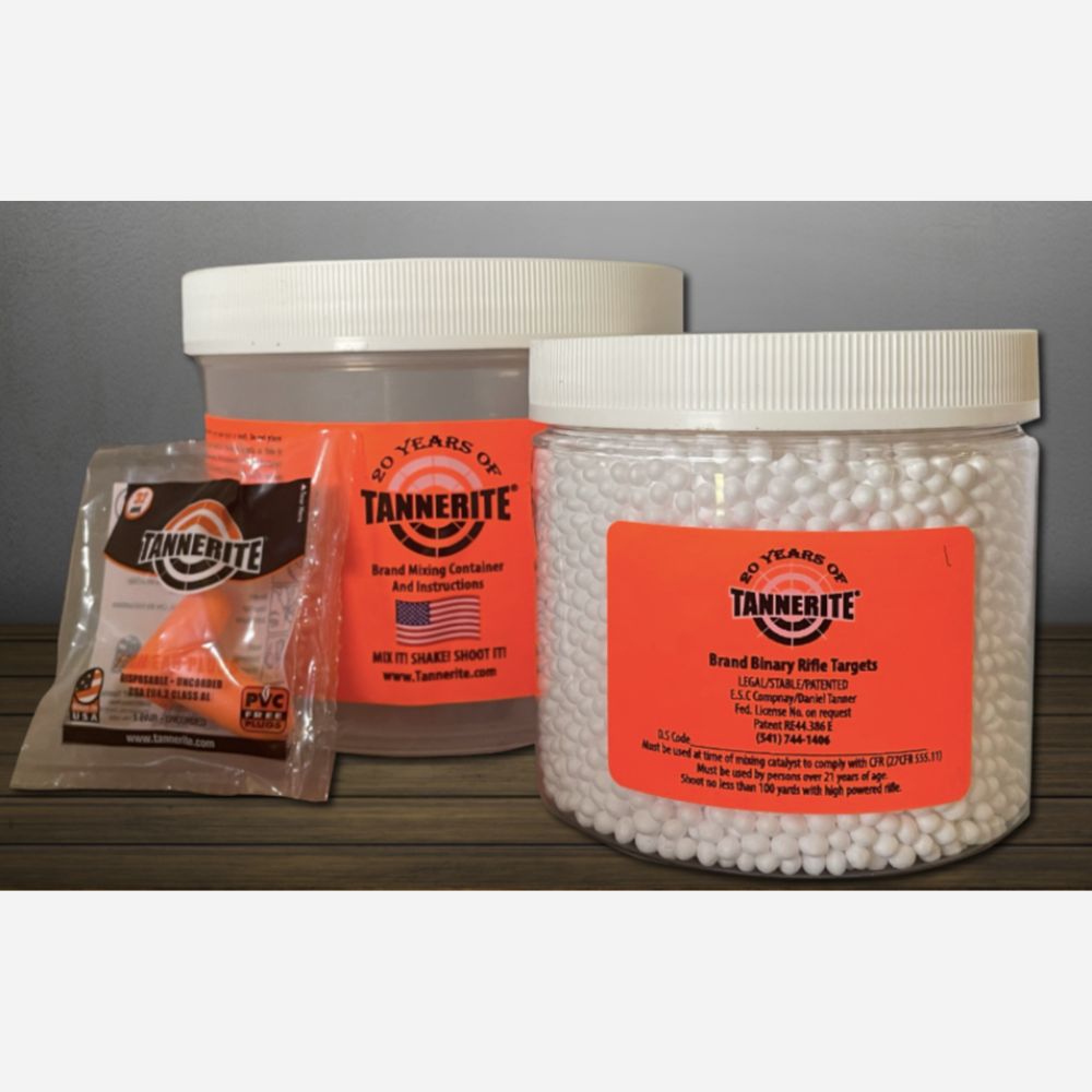 Two clear plastic jars of Tannelite Brand Binary Rifle Target foam pellets with white lids and bright orange labels, alongside a small sealed packet of Tannelite Brand Mixing Compound, displayed on a dark wooden surface against a gray background.