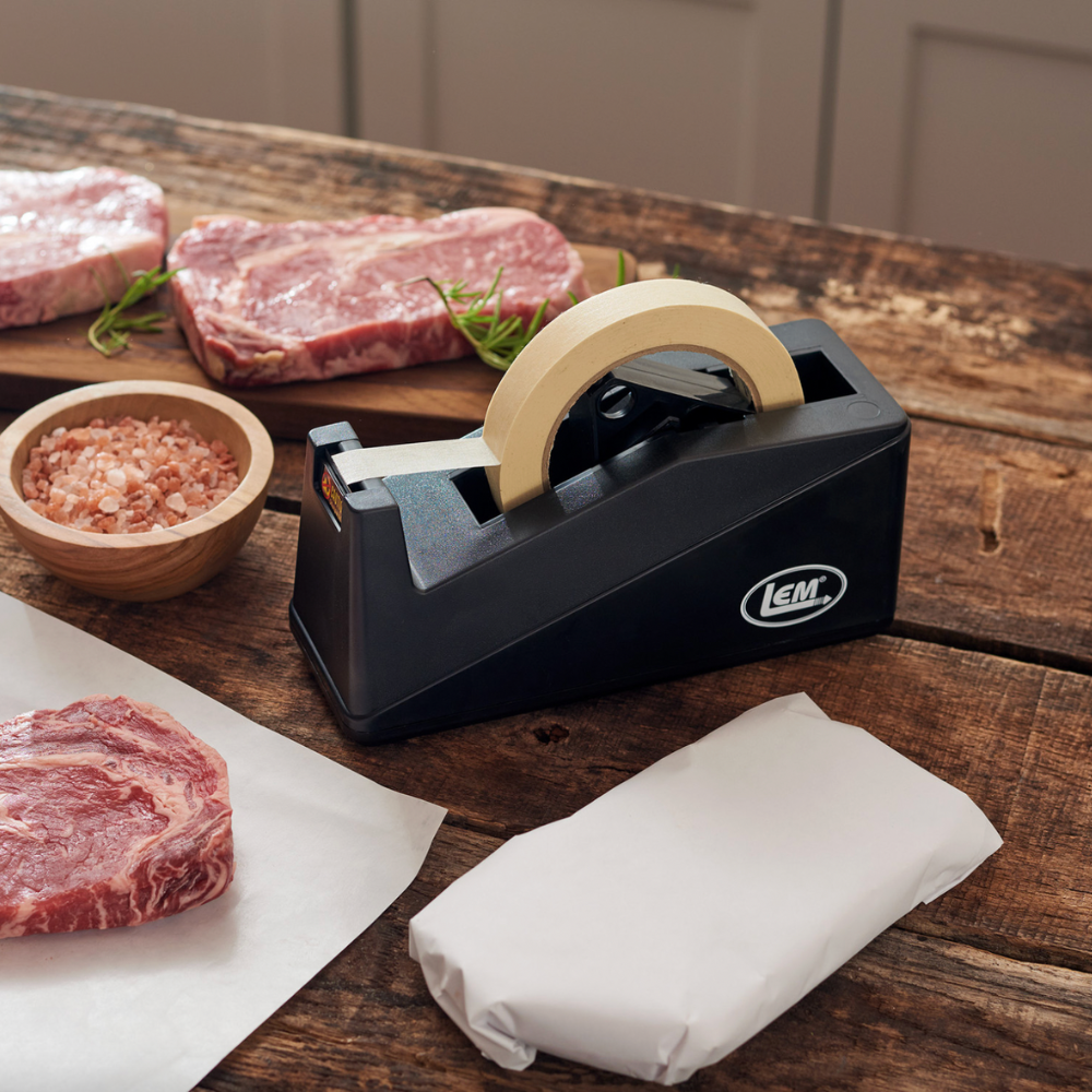 Black plastic wrap dispenser on a wooden table with raw meat and salt.