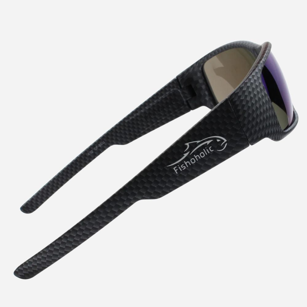 Black carbon-fiber-textured sunglasses with a white Fishoholic logo on the temple, shown against a light gray background.