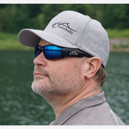 A man in profile wearing a heather gray Fishholic baseball cap and black sunglasses with blue mirrored lenses, set against a blurred background of water and green trees.