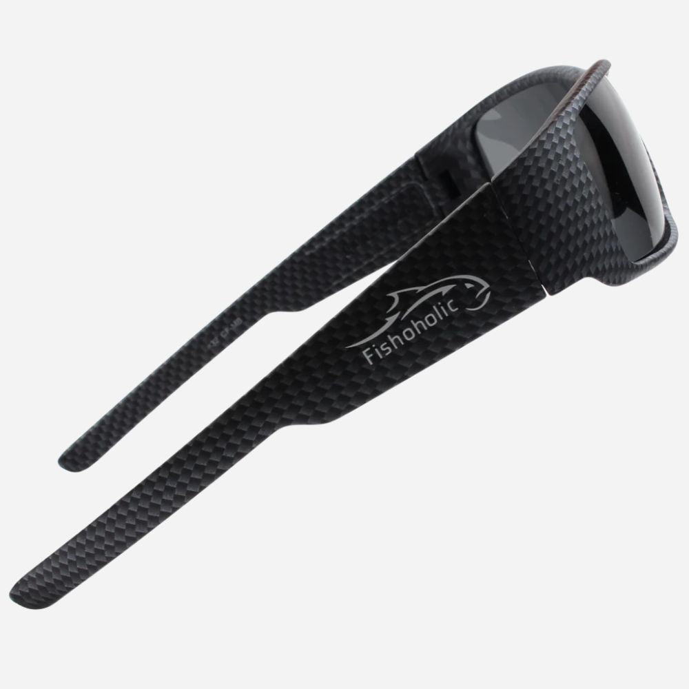 Black carbon fiber sunglasses with a glossy dark lens and the Fishoholic logo printed in white on the temple, shown on a light gray background.