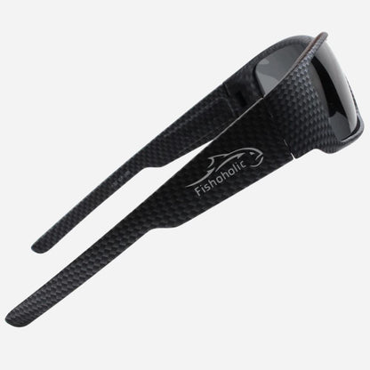 Black carbon fiber sunglasses with a glossy dark lens and the Fishoholic logo printed in white on the temple, shown on a light gray background.
