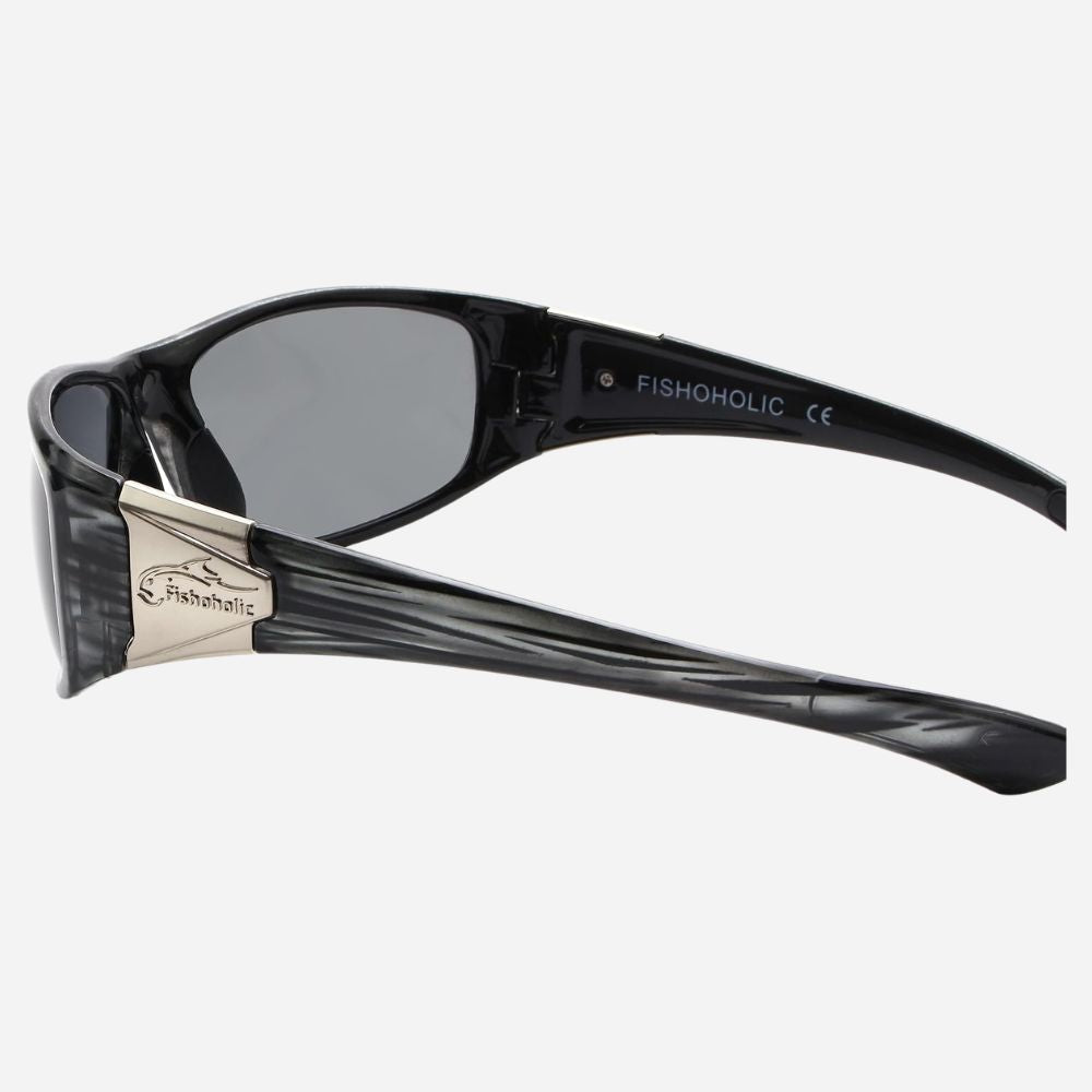 Fishoholic sunglasses with a black translucent frame, dark gray lenses, and a silver metal bridge accent, shown from a side angle on a light gray background.