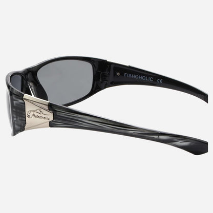 Fishoholic sunglasses with a black translucent frame, dark gray lenses, and a silver metal bridge accent, shown from a side angle on a light gray background.