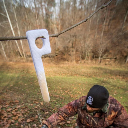 White scent wick hanging from a tree branch outdoors with person in camouflage in the background