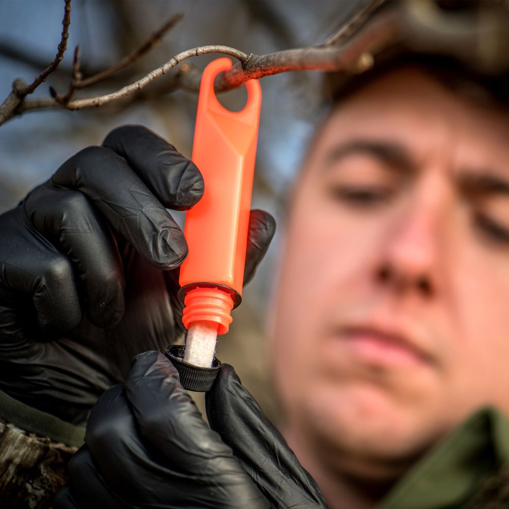 Person using an orange tool on a branch, wearing black gloves.