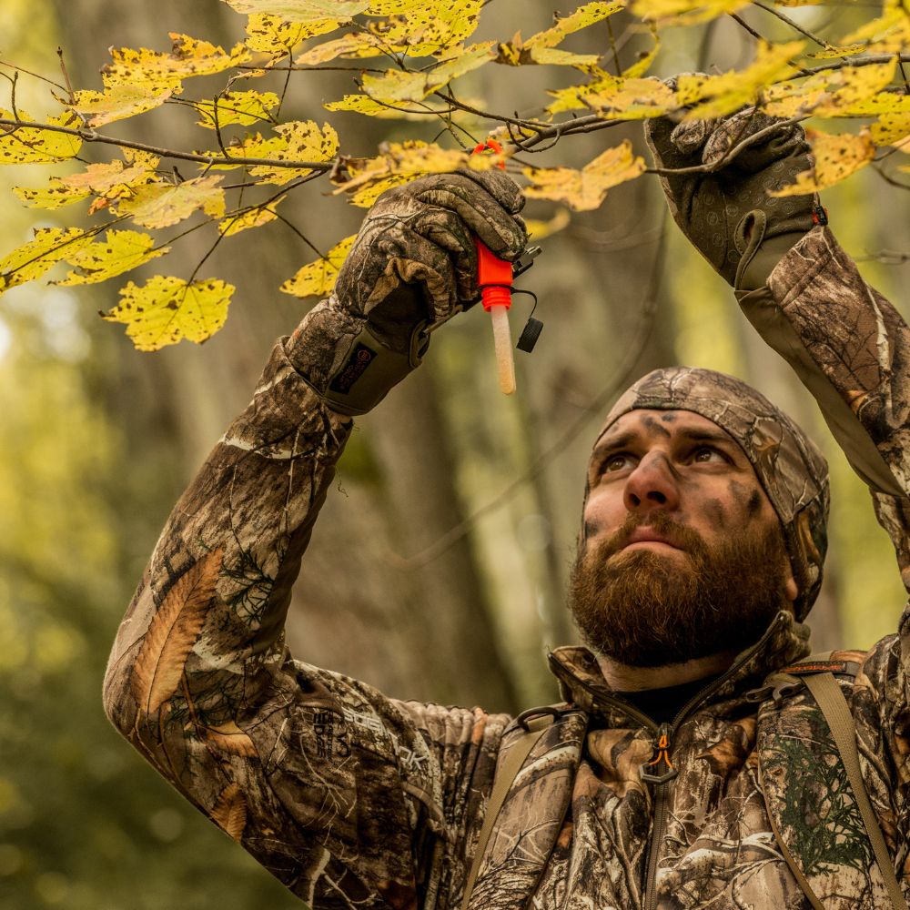 Man in camouflage gear holding a hunting call in a forest setting
