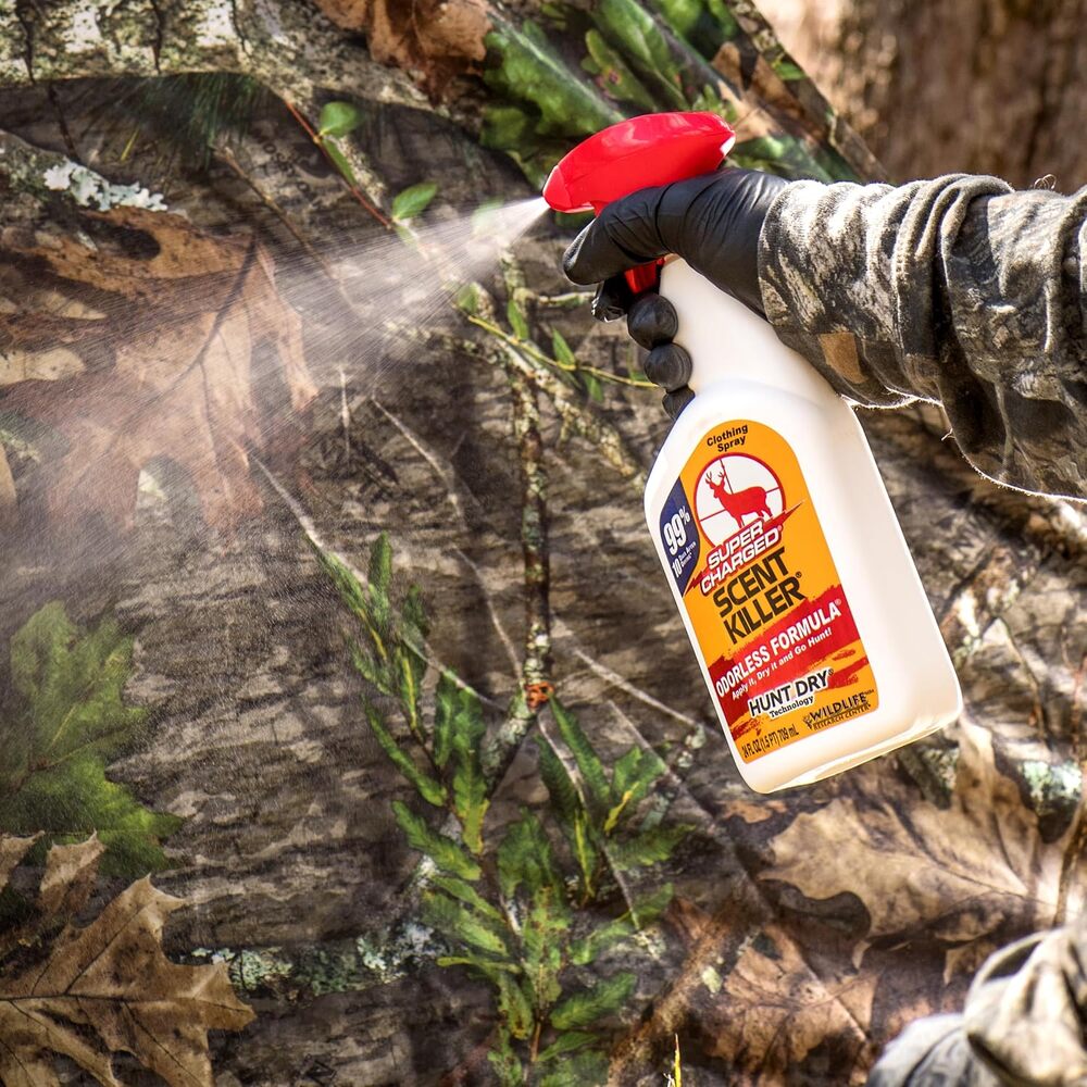 Person holding a bottle of 'Scout Killer' spray in a camouflage setting