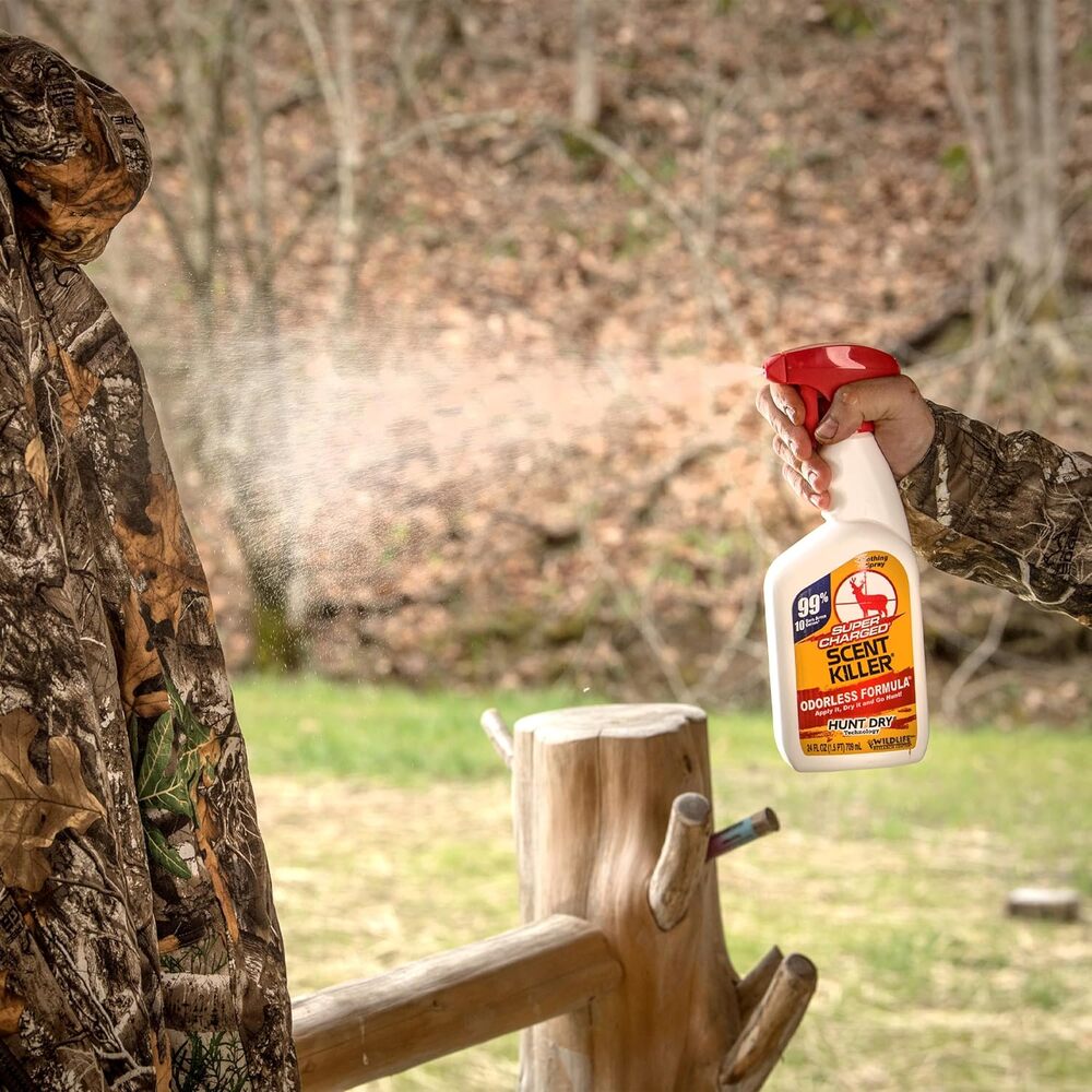 Person in camouflage holding a bottle of Scent Killer spray outdoors.