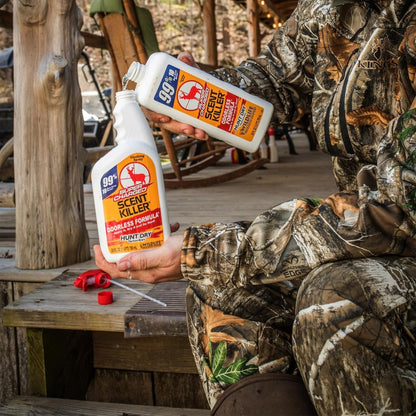 Person in camouflage holding two bottles of AGS Scent Killer in a rustic outdoor setting.