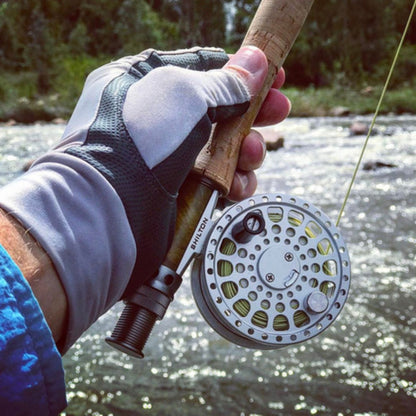 Fishing rod with reel held by a person wearing gloves, with a blurred natural background