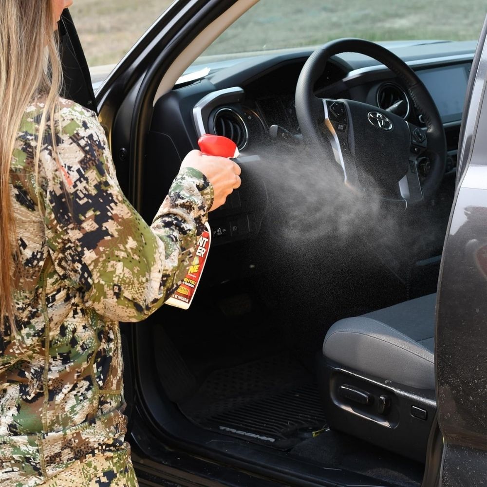 Person wearing camouflage spraying Scent Killer No Zone deodorizer inside a vehicle interior