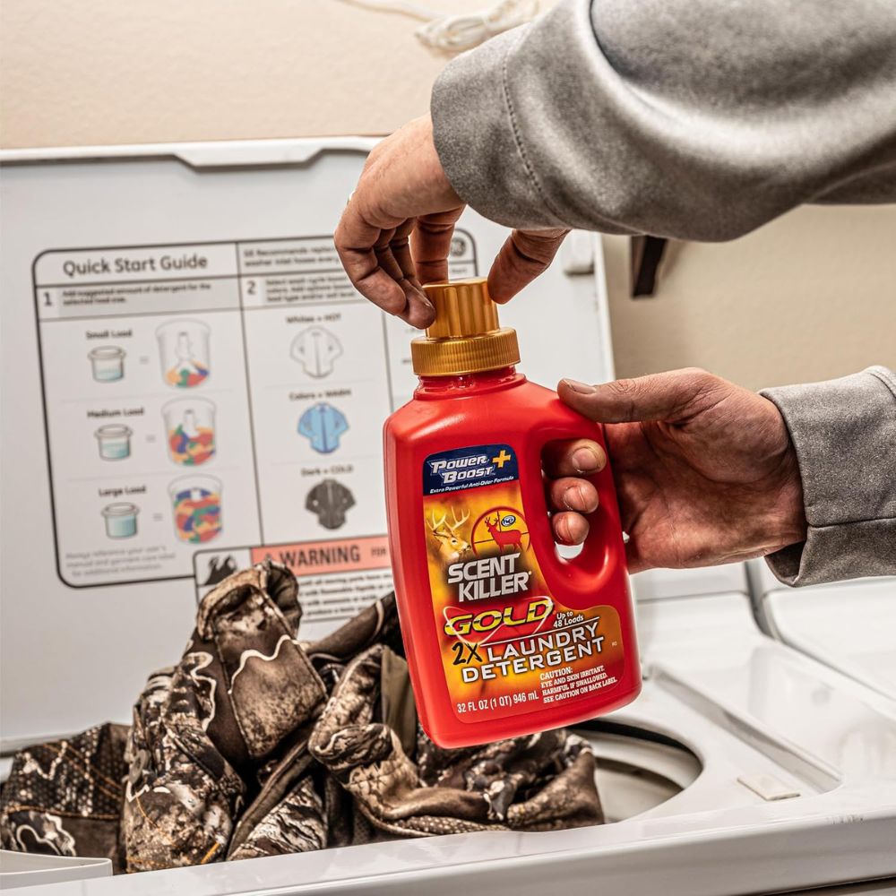 Person holding a bottle of Power Bright Scent Killer Gold laundry detergent above clothes in a washing machine.