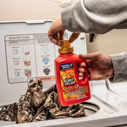 Person holding a bottle of Power Bright Scent Killer Gold laundry detergent above clothes in a washing machine.