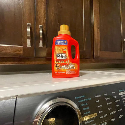 Red bottle of Power Bright Scent Killer Gold laundry detergent on a washing machine.