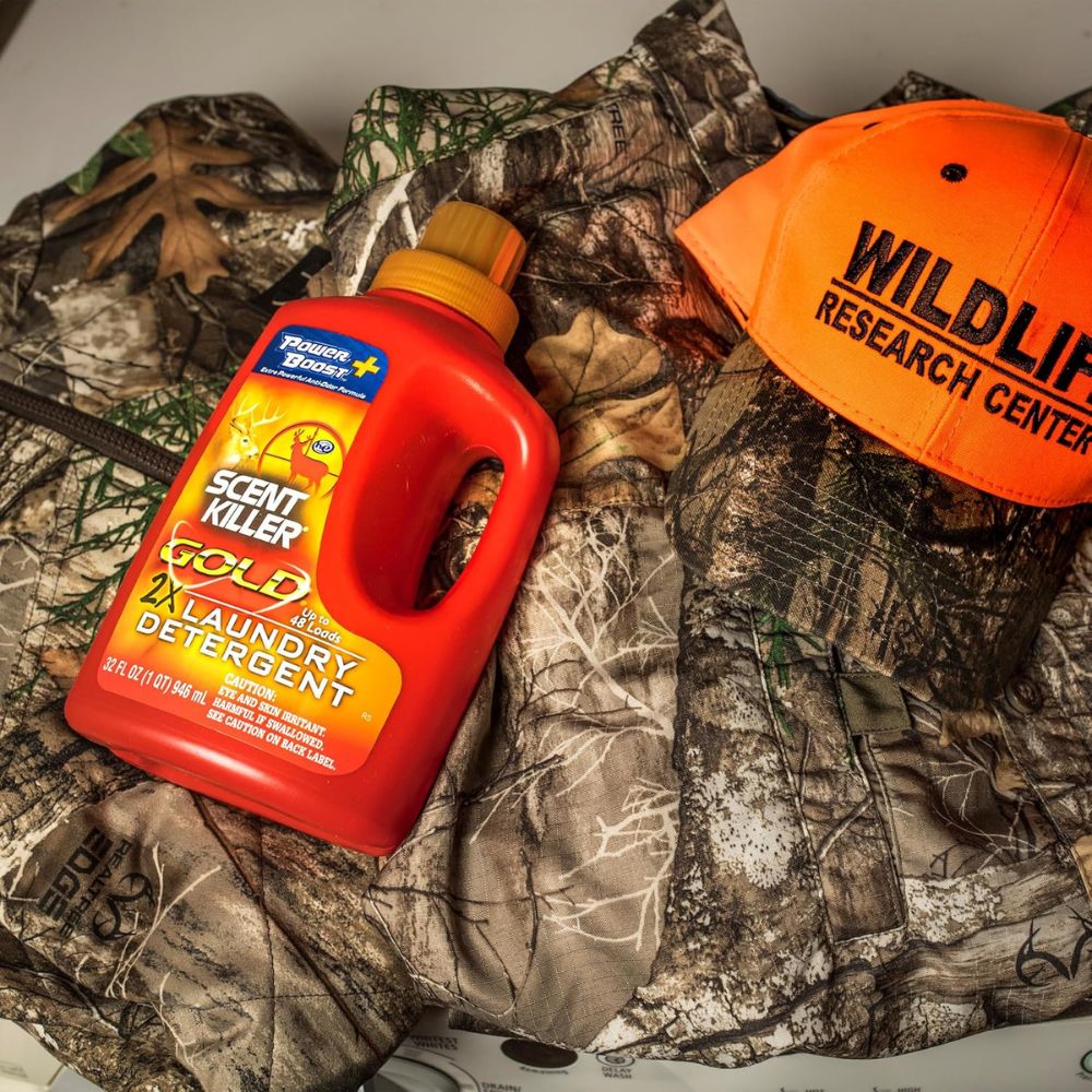 Red bottle of Power Bright laundry detergent on camouflage fabric with an orange cap labeled 'Wildlife Research Center'.