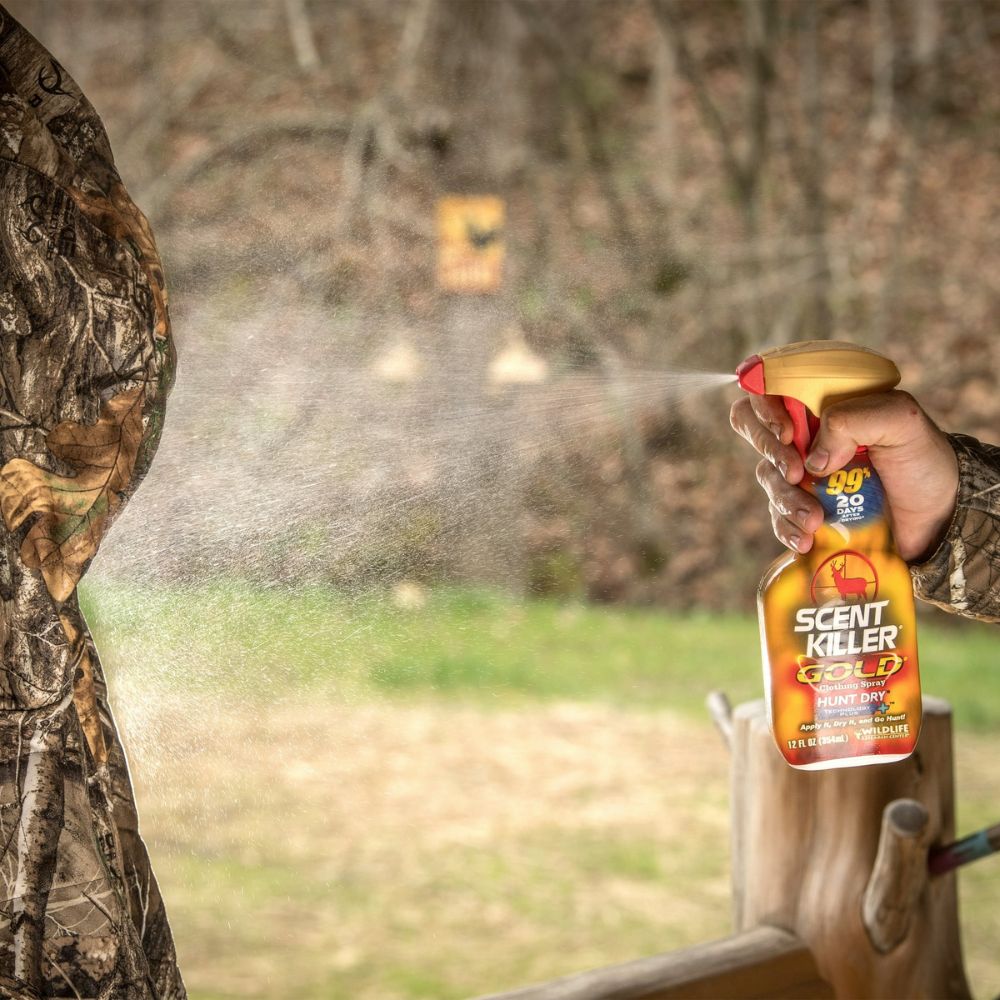 Person in camouflage holding a spray bottle labeled 'Scent Killer' outdoors.