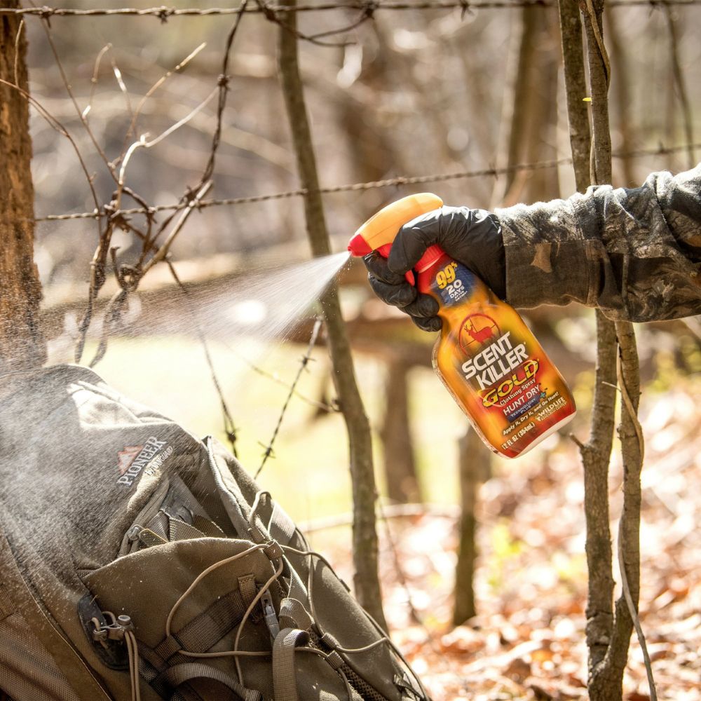 Person holding a Scent Killer Gold spray can in a forest setting