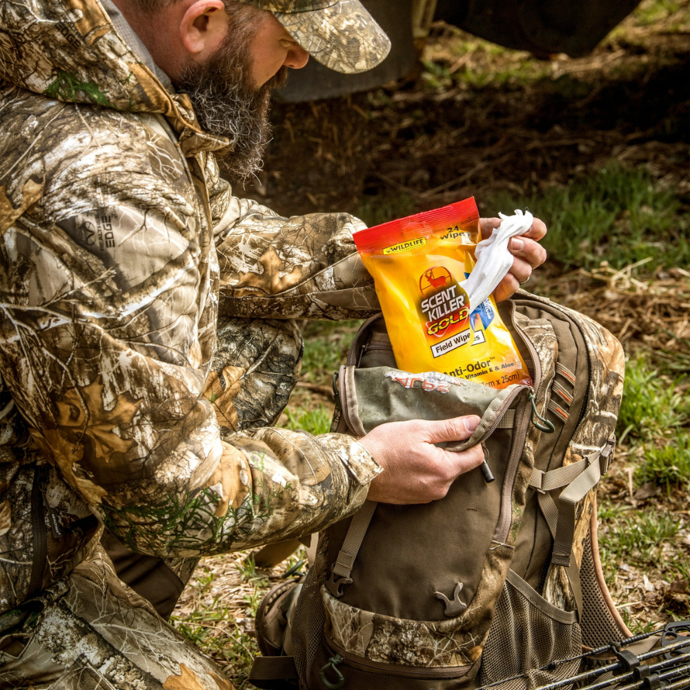 Person wearing camouflage clothing placing Scent Killer Gold field wipes into a backpack outdoors