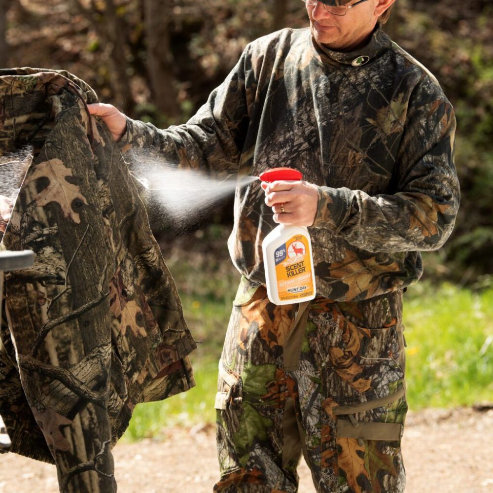 Person in camouflage clothing applying a spray product to a jacket outdoors.