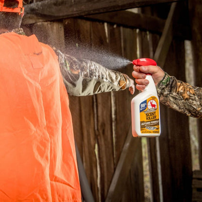 Person in camouflage holding a bottle of Scent Killer spray towards another person in an orange vest.