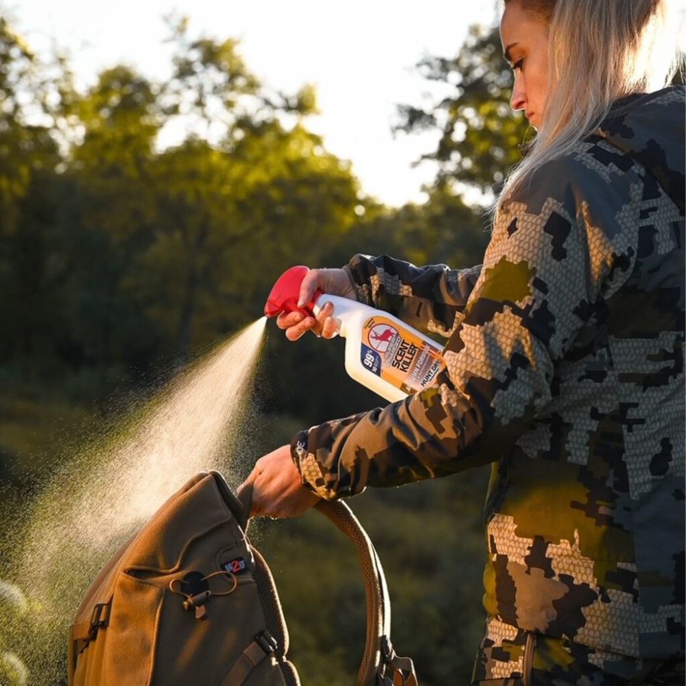Person in camouflage jacket using a spray bottle on a backpack outdoors