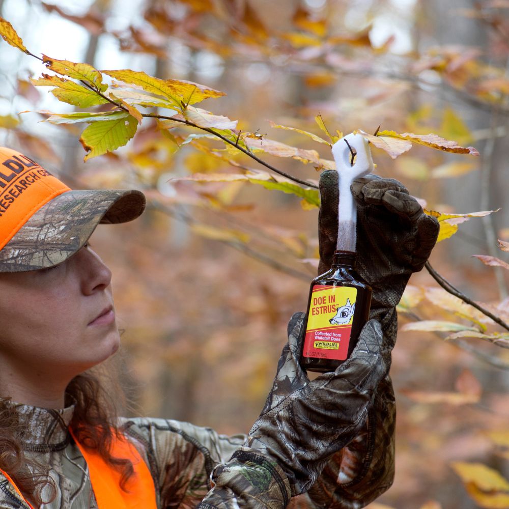 Person in hunting gear holding a bottle of 'Due In' Extreme in an autumn forest setting