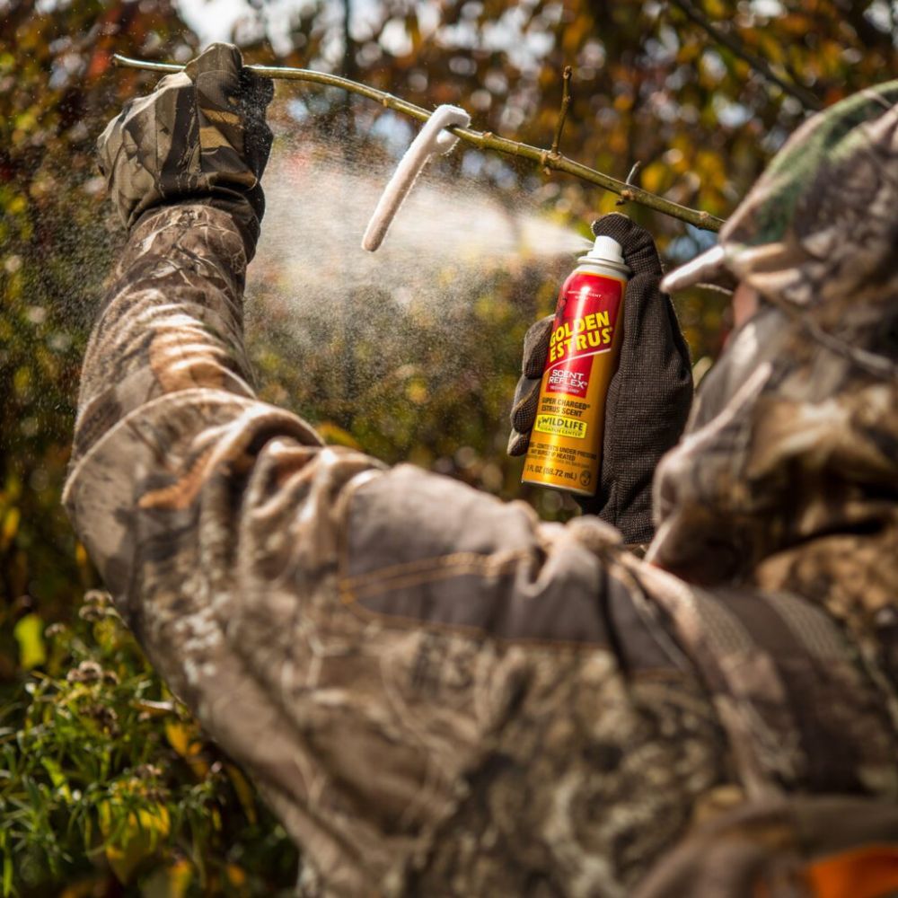 Person in camouflage holding a can of Golden Rabbit spray in a forest setting