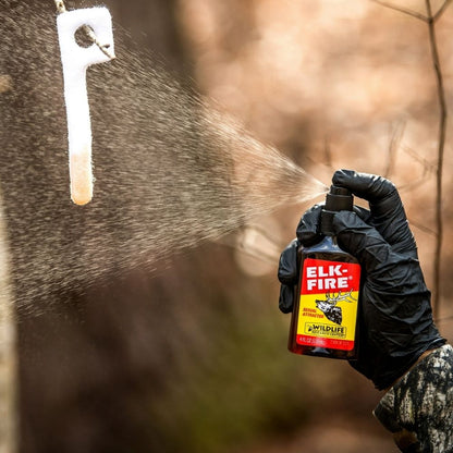 Gloved hand spraying Elk-Fire scent attractant onto hanging scent wick outdoors