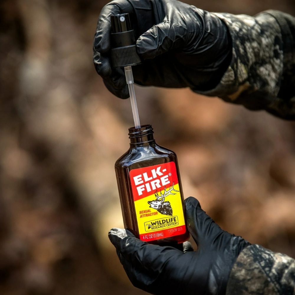 Gloved hands holding Elk-Fire scent attractant bottle with spray nozzle removed outdoors