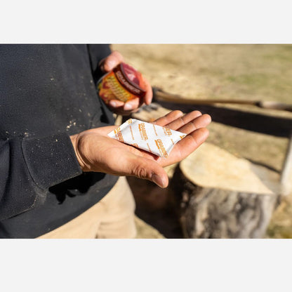 Person holding a white packet with orange text outdoors, possibly near water.