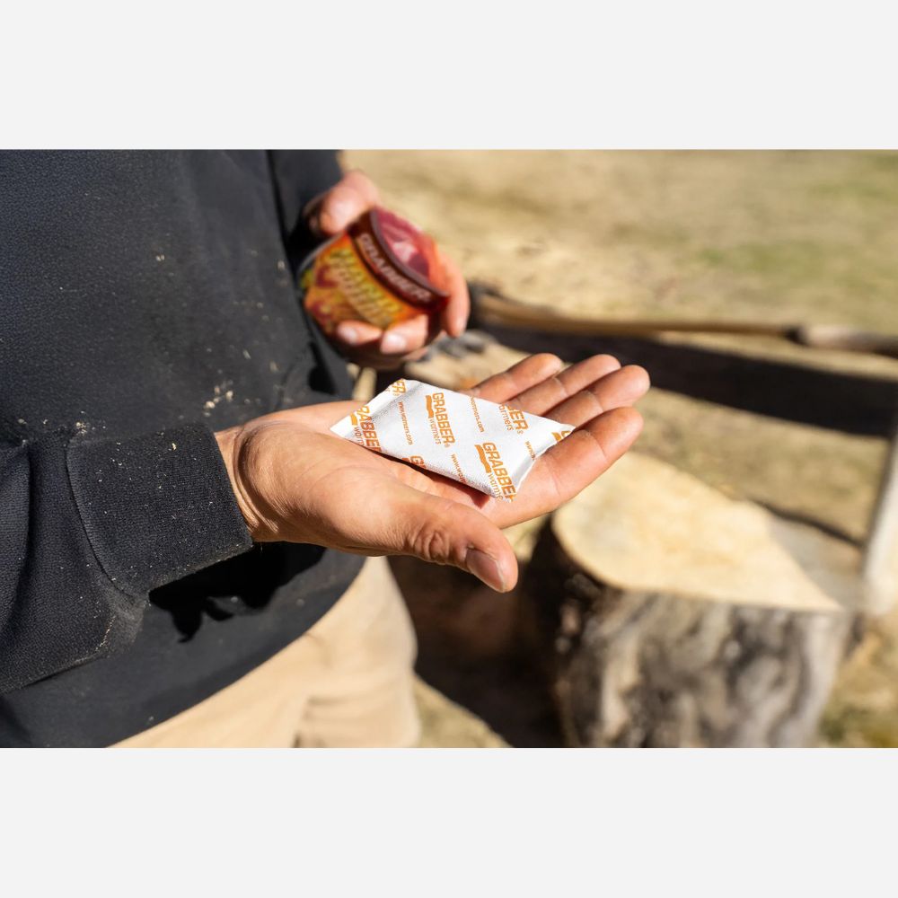 Person holding a bottle of hot sauce and a packet of seasoning outdoors.