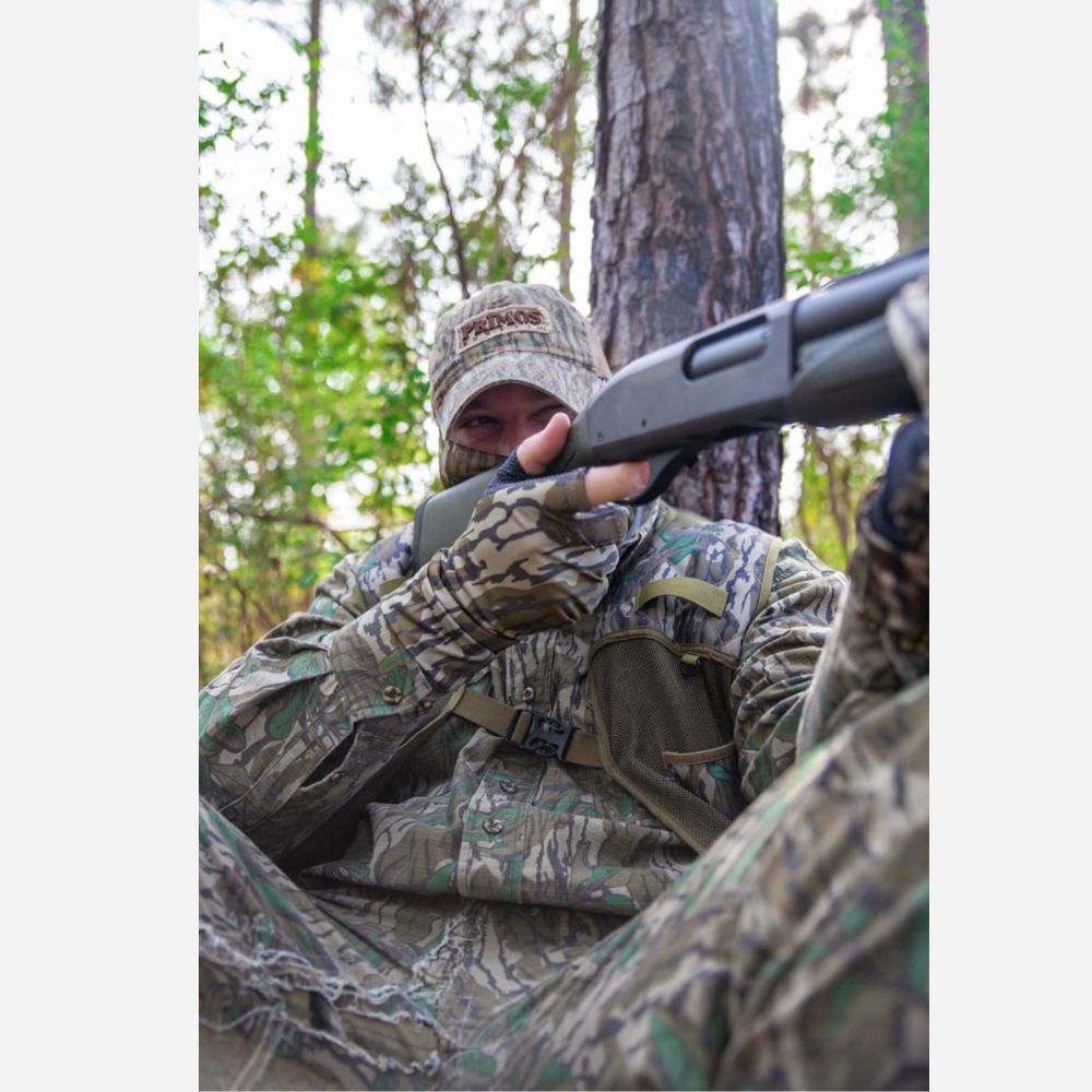Person in camouflage gear holding a shotgun in a forest setting