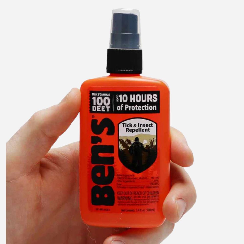 Hand holding an orange bottle of Ben's Tick & Insect Repellent with a white background