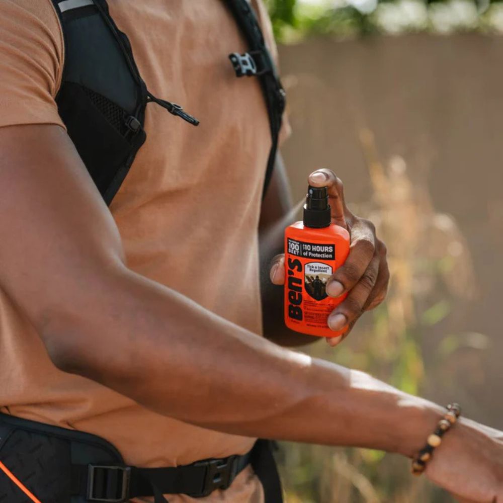 Person holding an orange insect repellent bottle outdoors