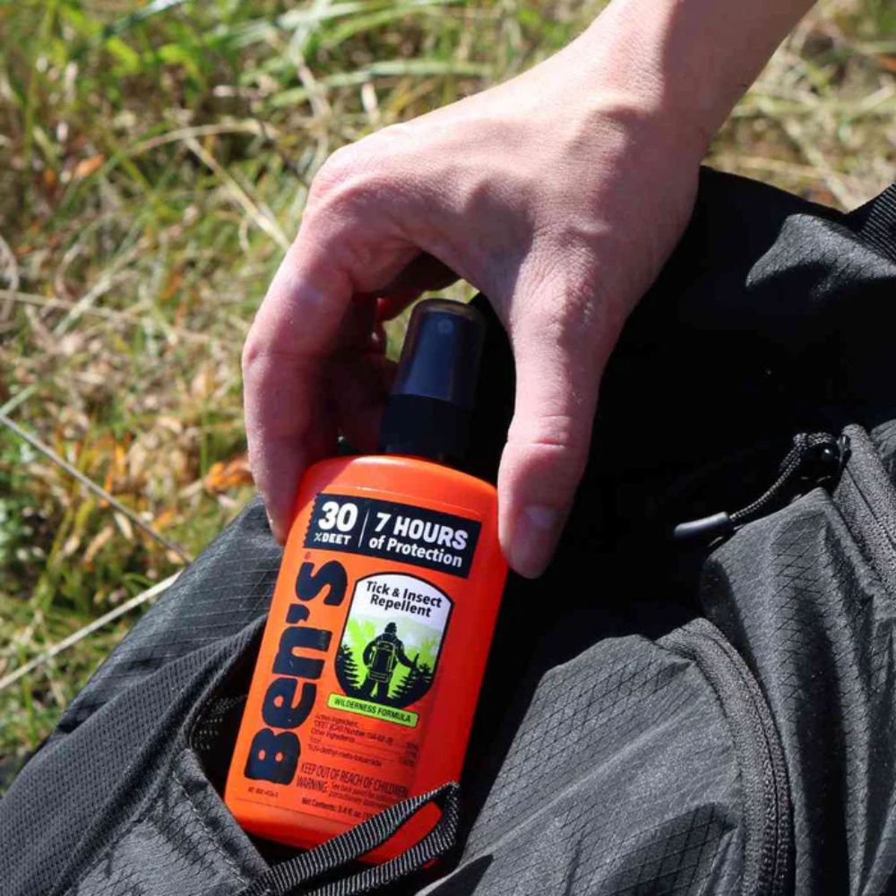 Person holding a bottle of Ben's insect repellent in a grassy outdoor setting