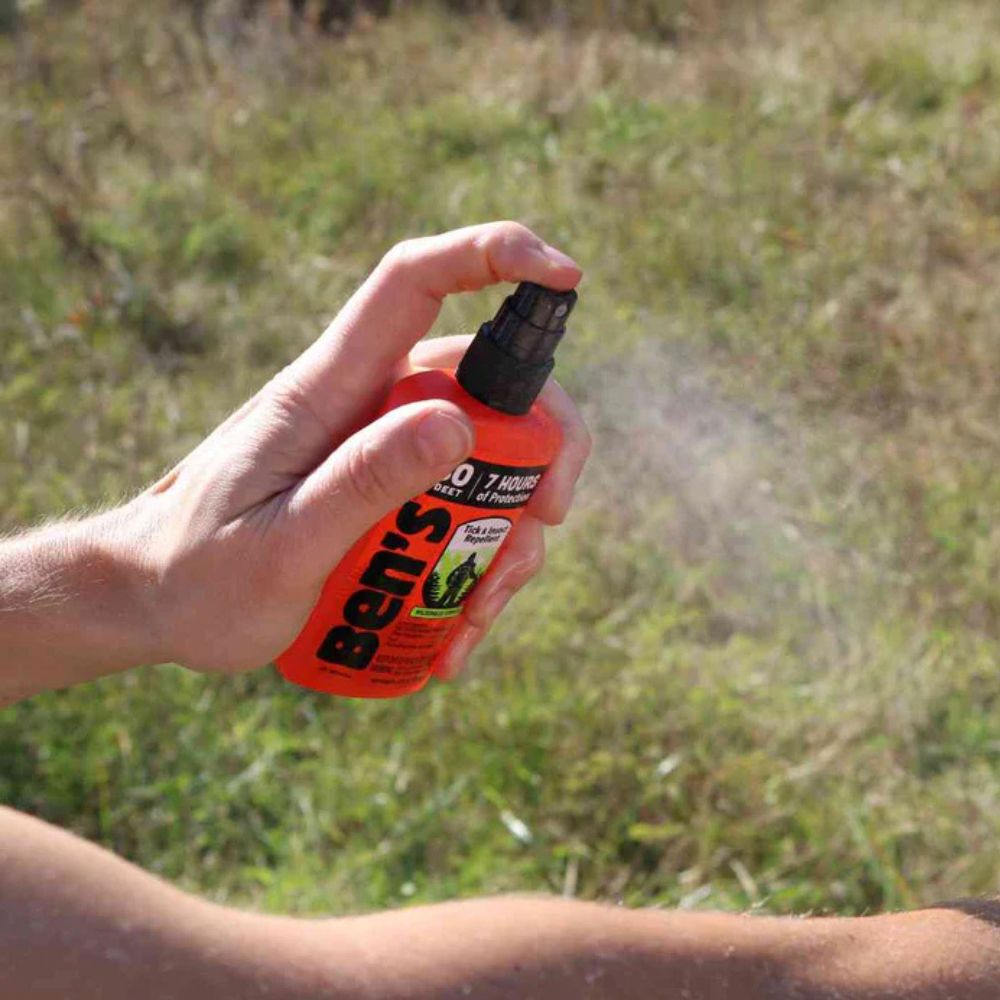 Person holding a bottle of Ben's insect repellent in an outdoor setting.