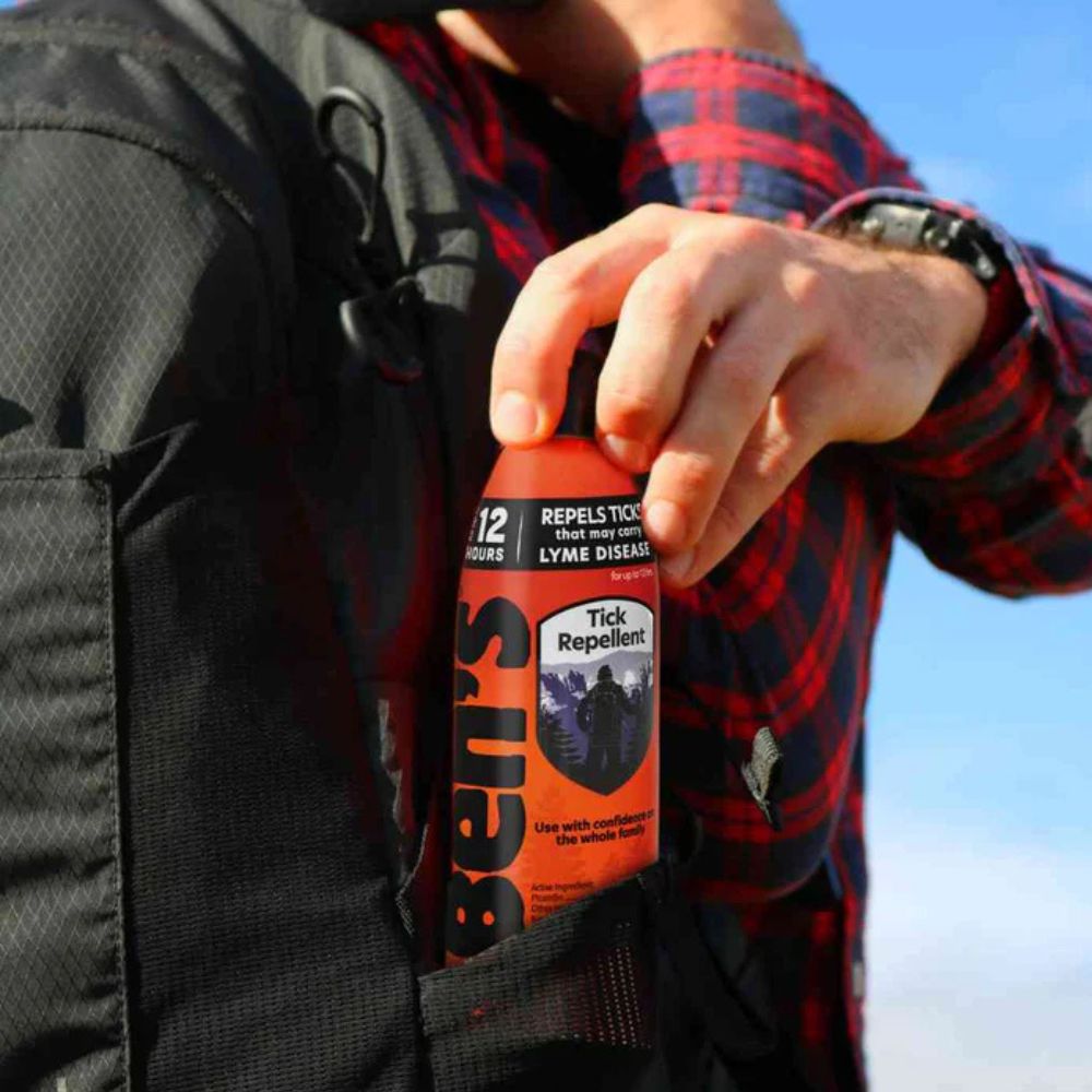 Person holding a bottle of Bel's Tick Repellent against a clear blue sky.