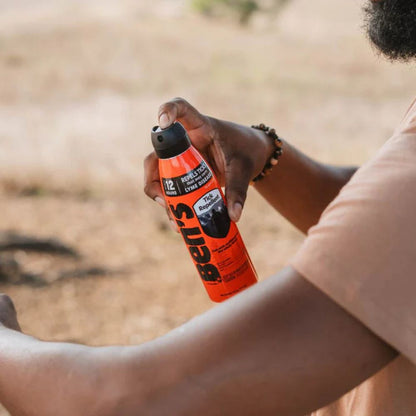 Person holding a can of Belts insect repellent spray outdoors.