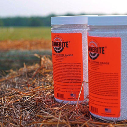 Two clear plastic jars of Bunkerite No. 8 Extreme Range powder with bright orange labels, placed on a bed of straw outdoors with a blurred field in the background.