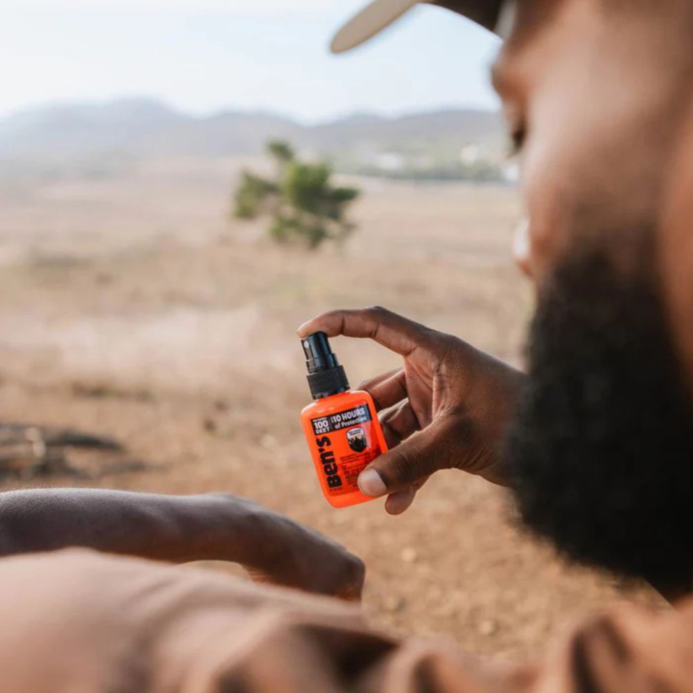 Person holding an orange spray bottle with a desert landscape in the background