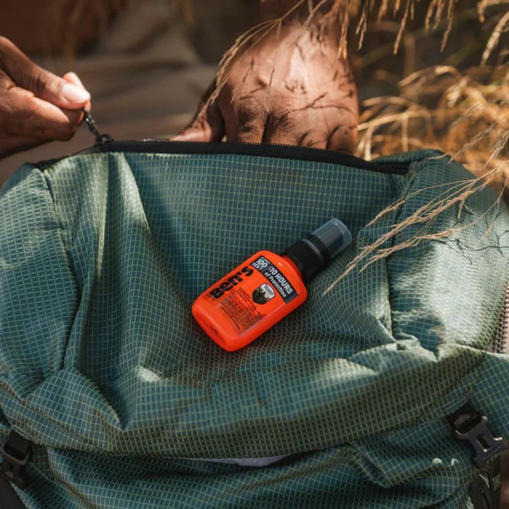 Orange BARTS water bottle on a green backpack with a person lying in the background.