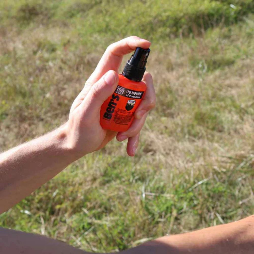 Hand holding an orange spray bottle with a grassy background