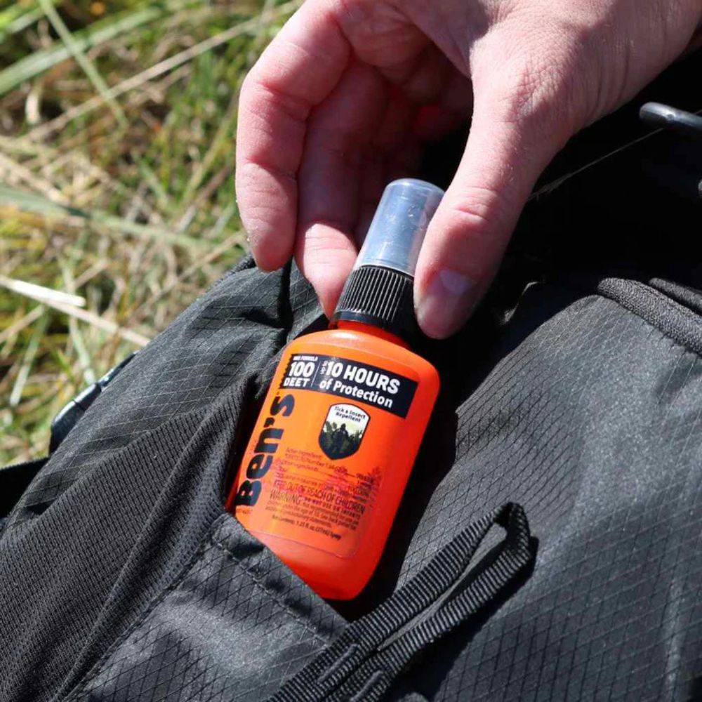 Person placing an orange bottle of Ben's insect repellent into a pocket with grass in the background