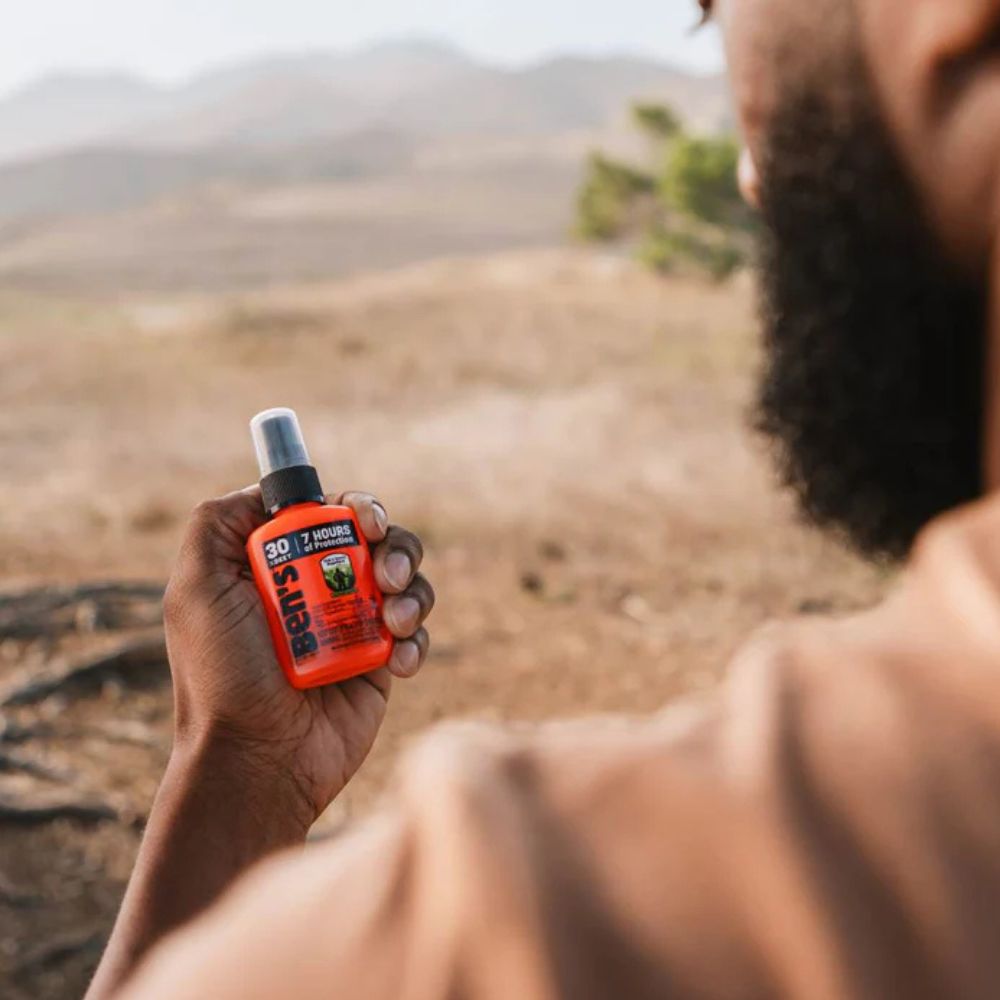 Person holding a bottle of Bear Spray in a natural outdoor setting