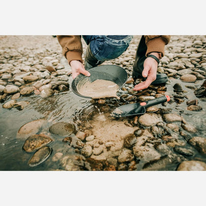 Person holding a metal detector over water with rocks and stones on the ground.