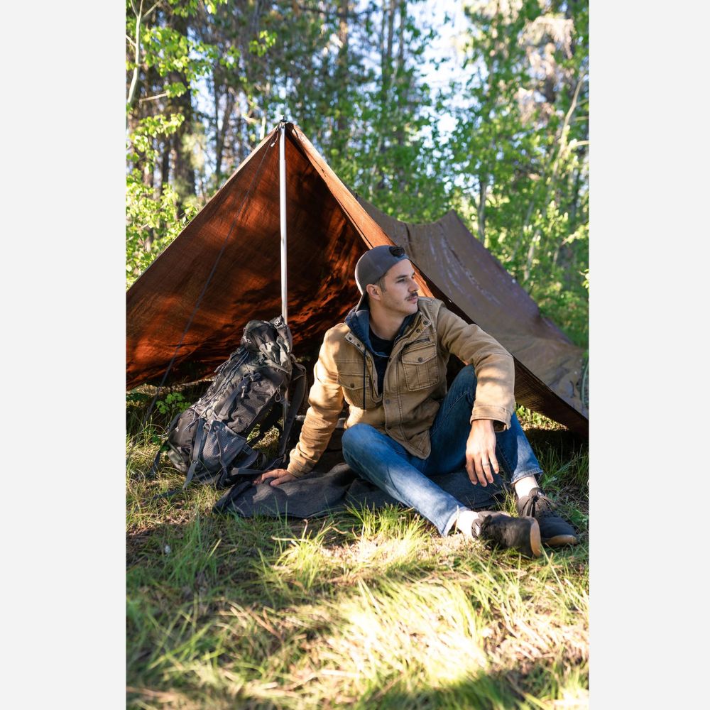 Man sitting in front of a small tent in a forest setting